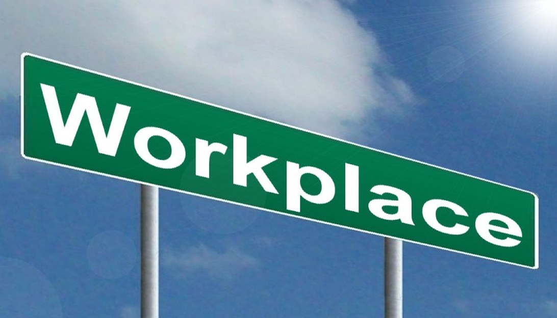 En grön gatuskylt med texten 'Workplace' mot en blå himmel med moln, symboliserar arbetsplatsen som en plats för gemenskap och stöd.