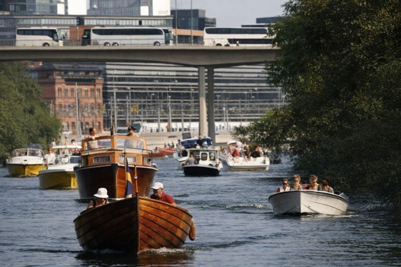 Båtar på vattnet under en bro, med byggnader i bakgrunden.